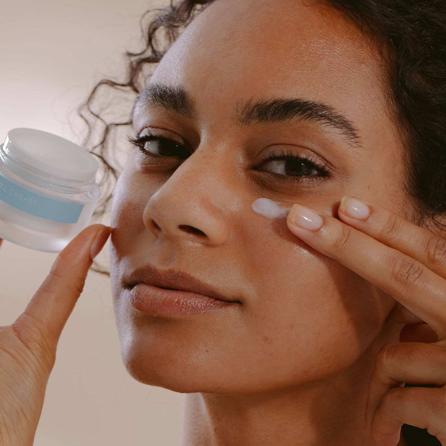 A woman applying Total Restorative Eye Cream from the Complete Complexion Kit by Cosmedica Skincare, highlighting skincare routine and hydrating benefits.