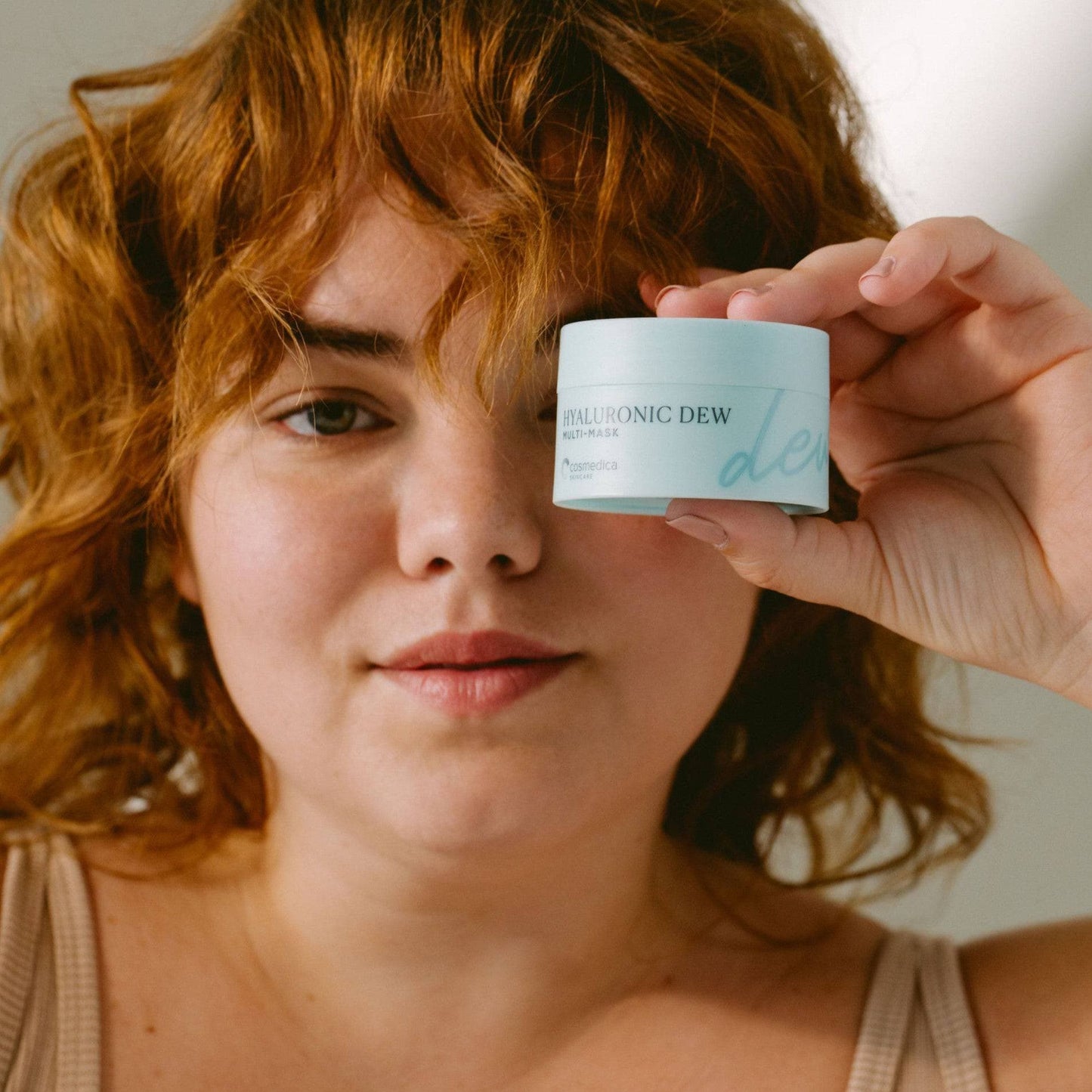 A person holding a container of Hyaluronic Dew Multi-Mask from Cosmedica Skincare, demonstrating its use for achieving hydrated skin.