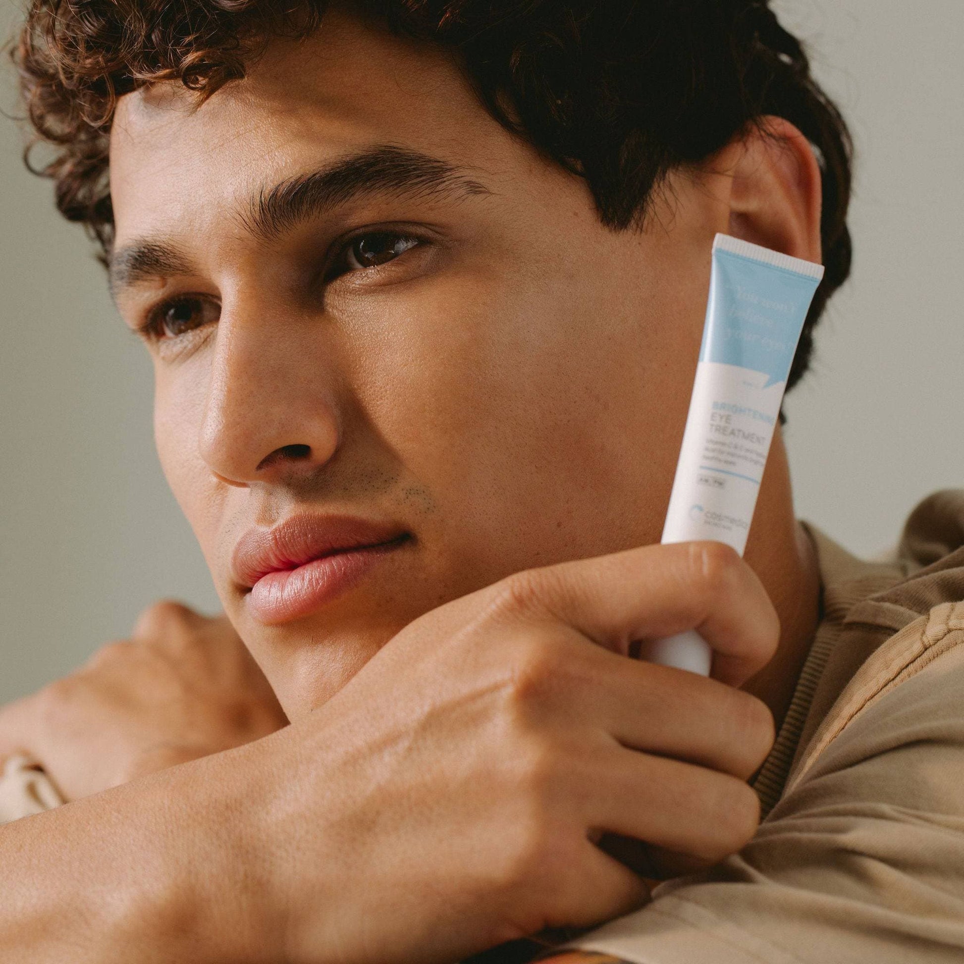 A thoughtful man holding Cosmedica Skincare's Brightening Eye Treatment Gel, emphasizing the effective eye care solution in a relaxed setting.