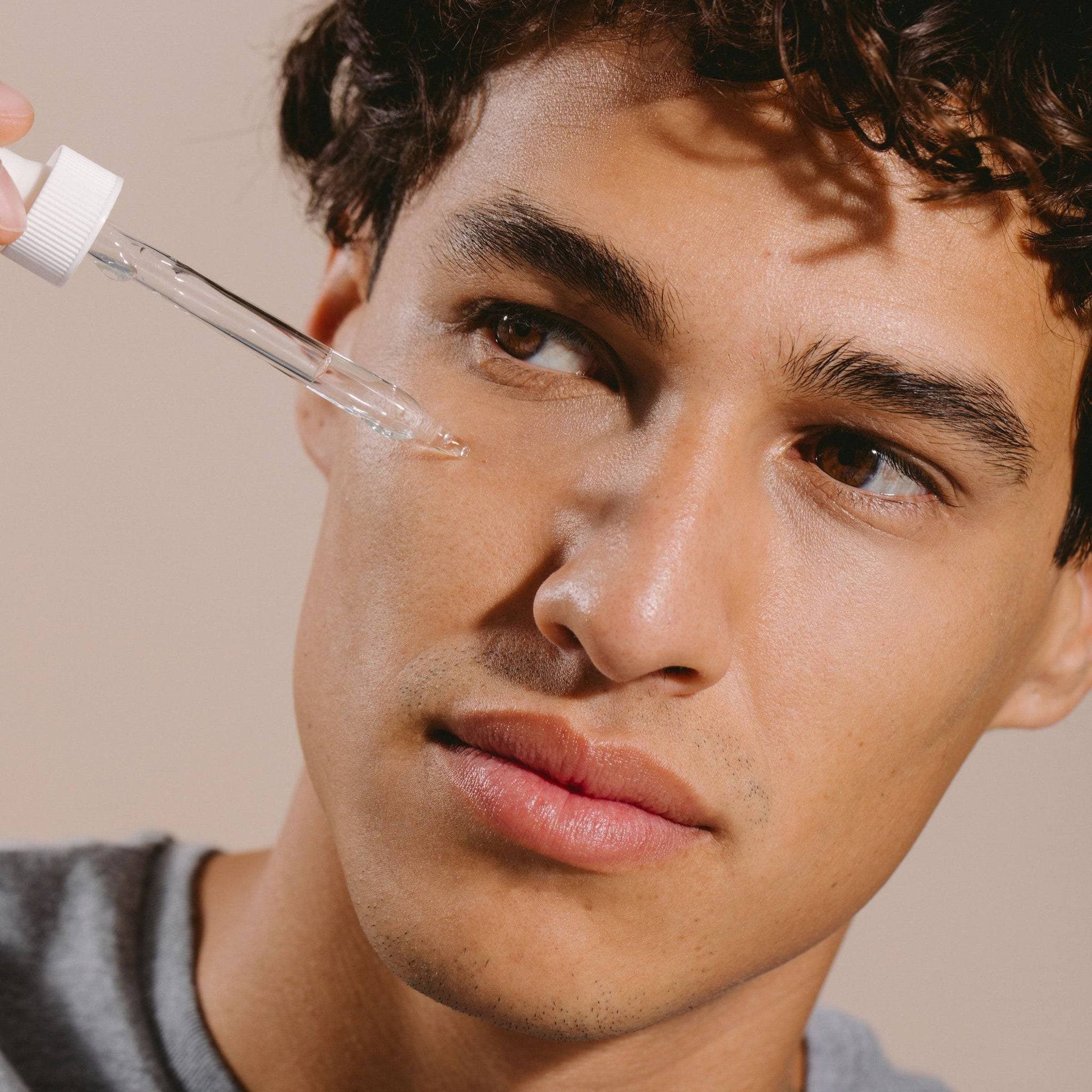 Man applying serum from a dropper onto his face, highlighting the use of Hyaluronic + Vitamin C Serum Set from Cosmedica Skincare.