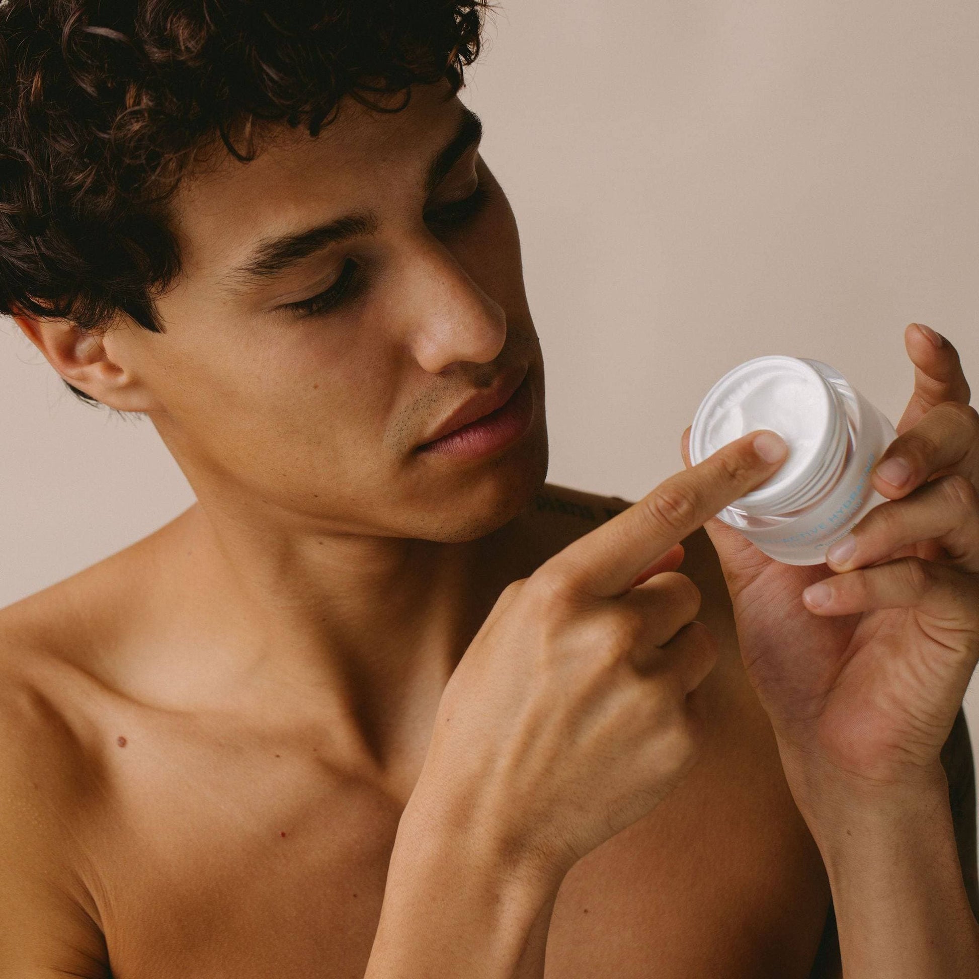 A man applying Cosmedica Skincare’s Multi-Active Hydrating Night Cream with a focused expression, showcasing the product's luxurious texture.