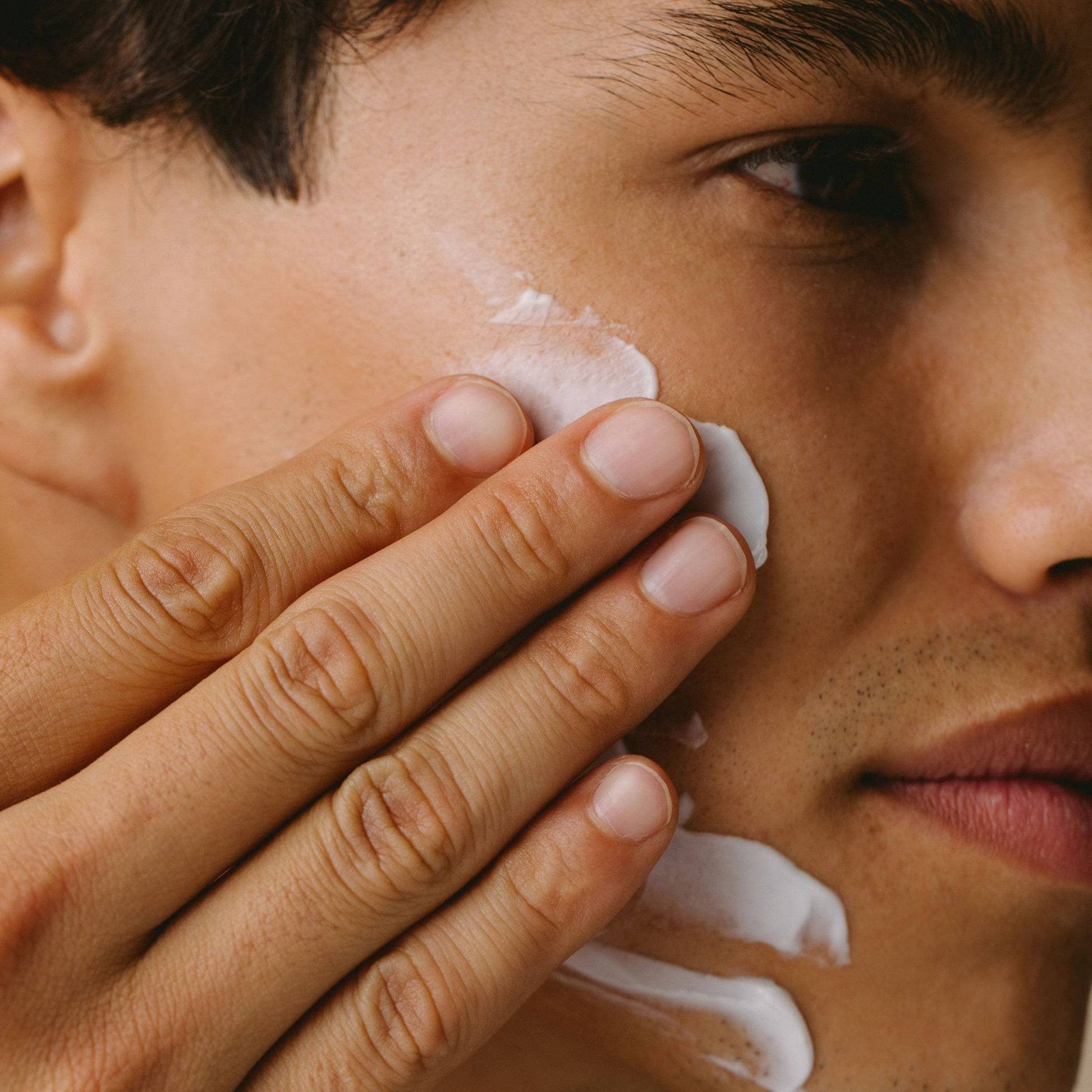 A close-up of a man gently smoothing Cosmedica Skincare’s Multi-Active Hydrating Night Cream onto his cheek, highlighting the nourishing properties of the cream.