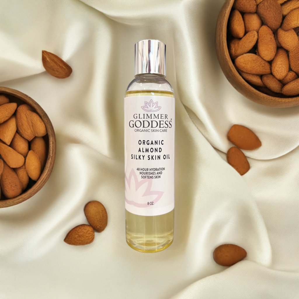Glimmer Goddess Organic Sweet Almond Silky Skin Oil featured with almonds on a fabric background, highlighting its natural ingredients and moisturizing benefits.