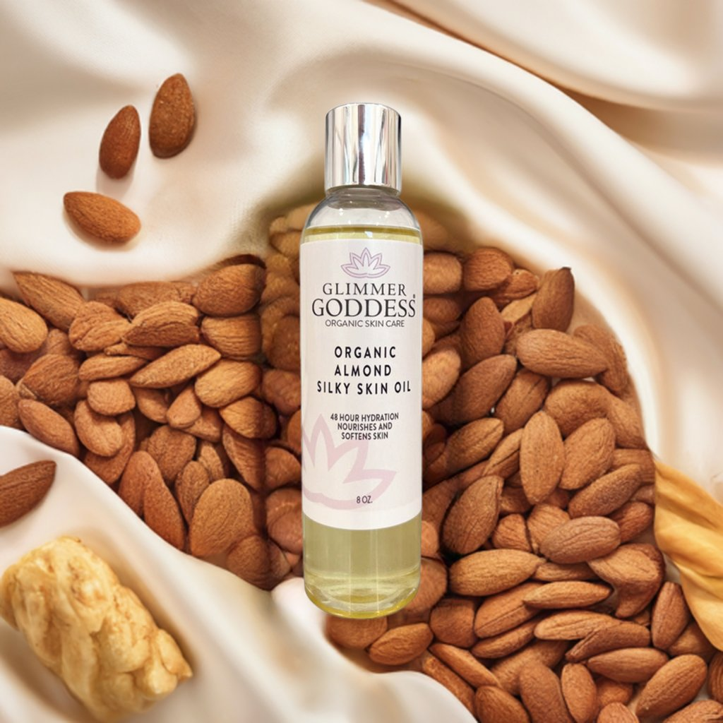 Glimmer Goddess Organic Sweet Almond Silky Skin Oil surrounded by raw almonds, emphasizing natural ingredients and long-lasting skin nourishment.