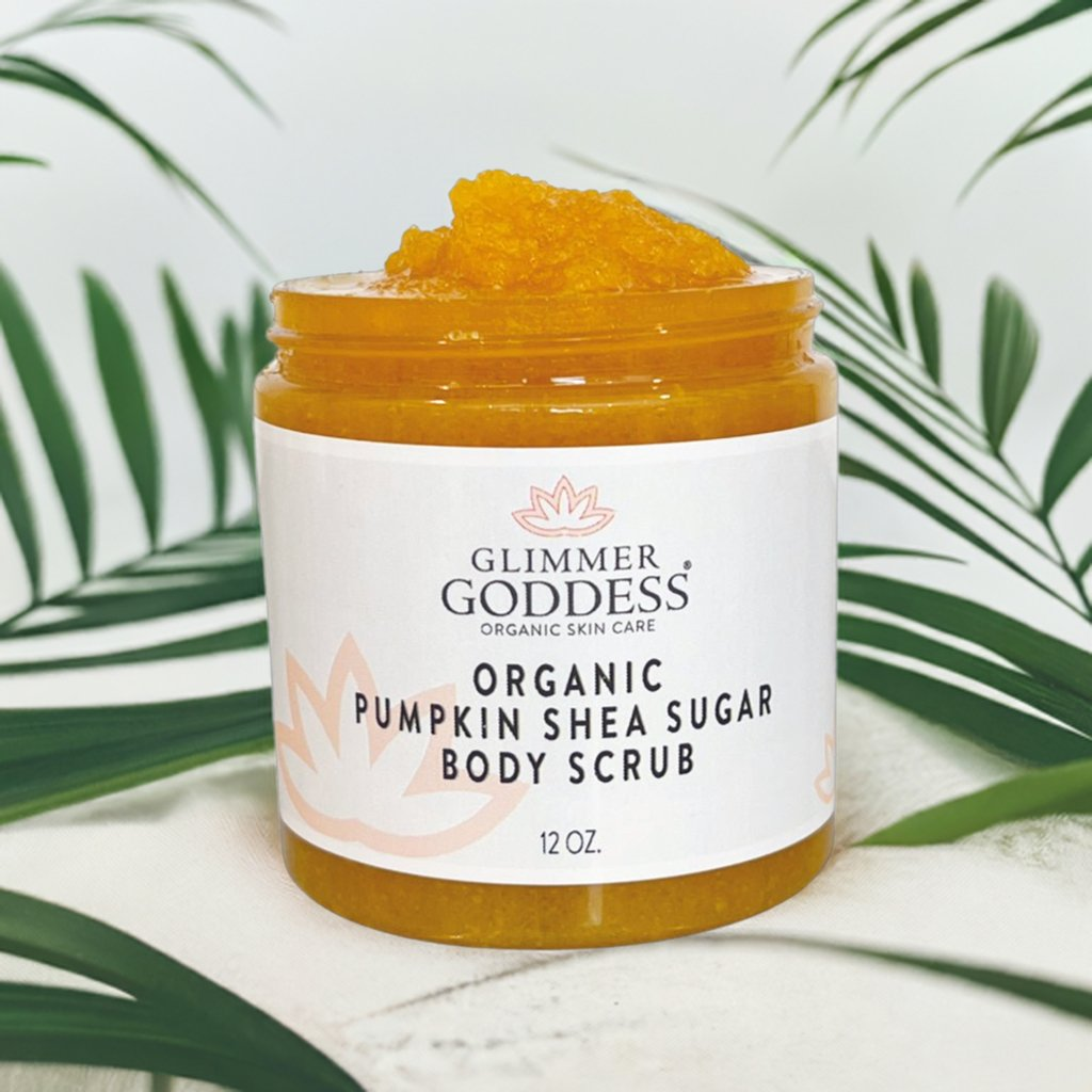 Glimmer Goddess Organic Pumpkin Shea Sugar Body Scrub jar with tropical leaves in the background, emphasizing its natural and organic ingredients.