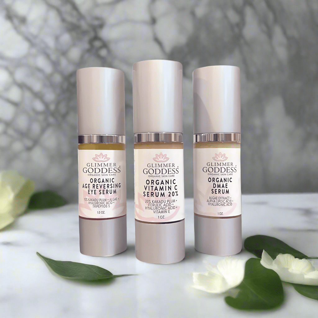 Glimmer Goddess Organic Anti-Aging Trio on a marble background, featuring the Age Reversing Eye Serum, Vitamin C Serum 20%, and DMAE, perfect for achieving glowing skin.