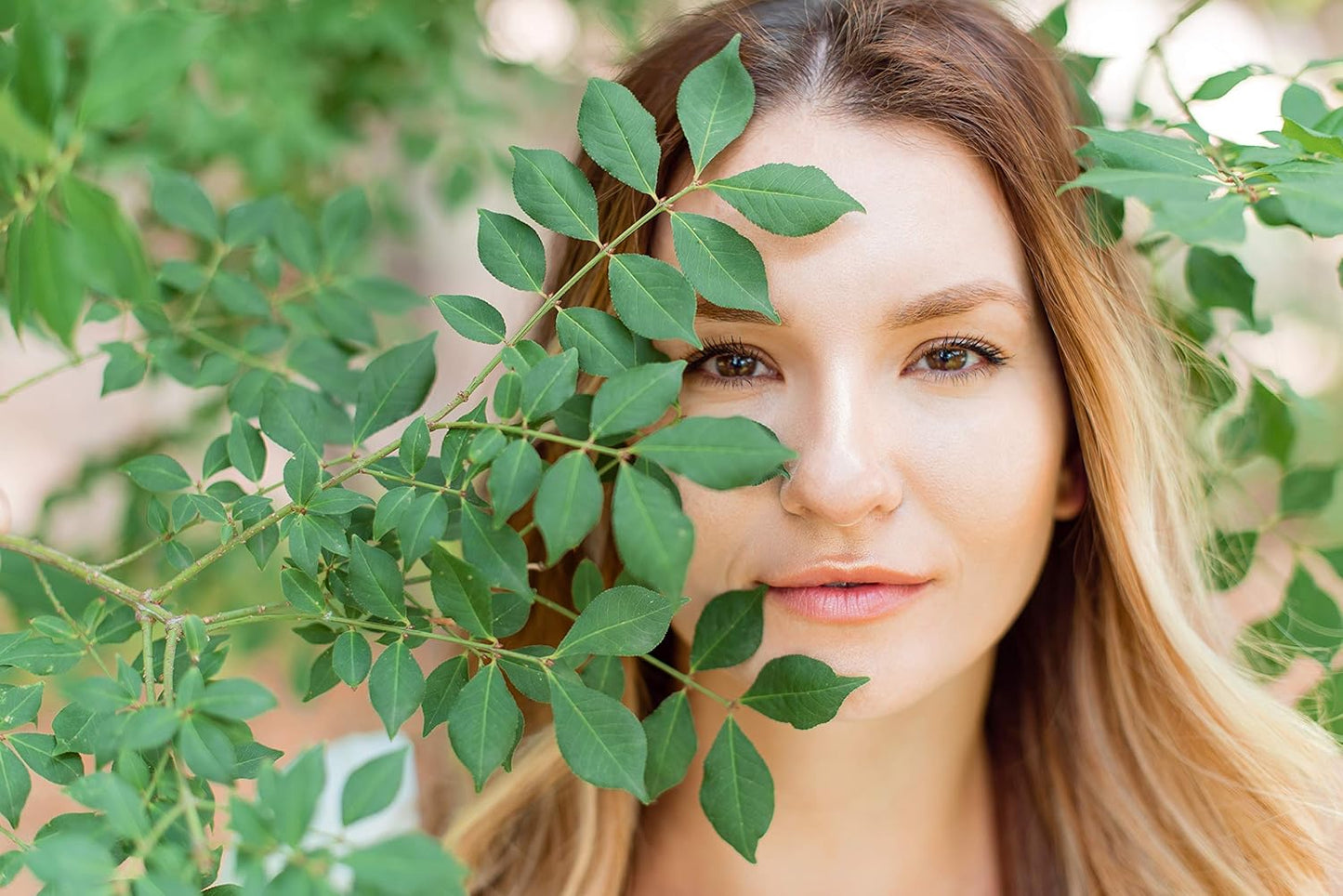 Close-up of a woman with a radiant complexion, partially hidden by green leaves, showcasing healthy skin, featuring Cosmedica Skincare's 2.5% Retinol Facial Night Cream.