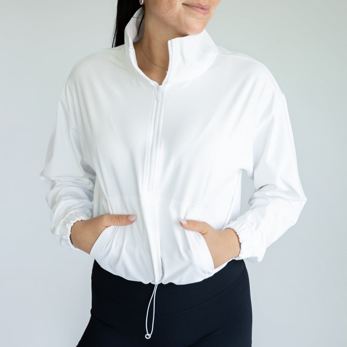 Elegant woman dressed in a white Ascend 1/4 Zip Jacket by DYM Athletics, highlighting the jacket’s lightweight fabric and sporty aesthetic.