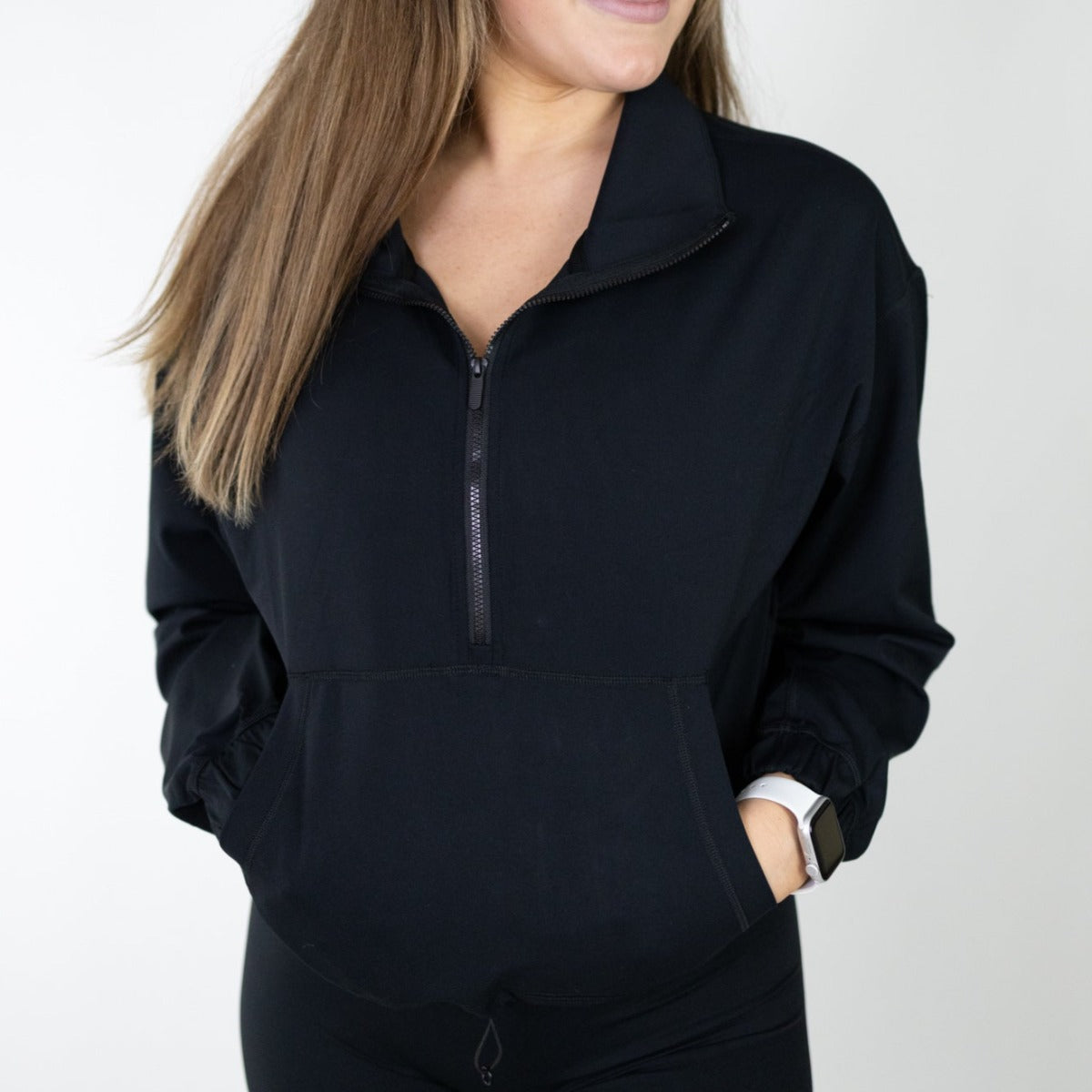 Woman sporting a sleek black Ascend 1/4 Zip Jacket by DYM Athletics, featuring a cozy front pocket and stylish silhouette.
