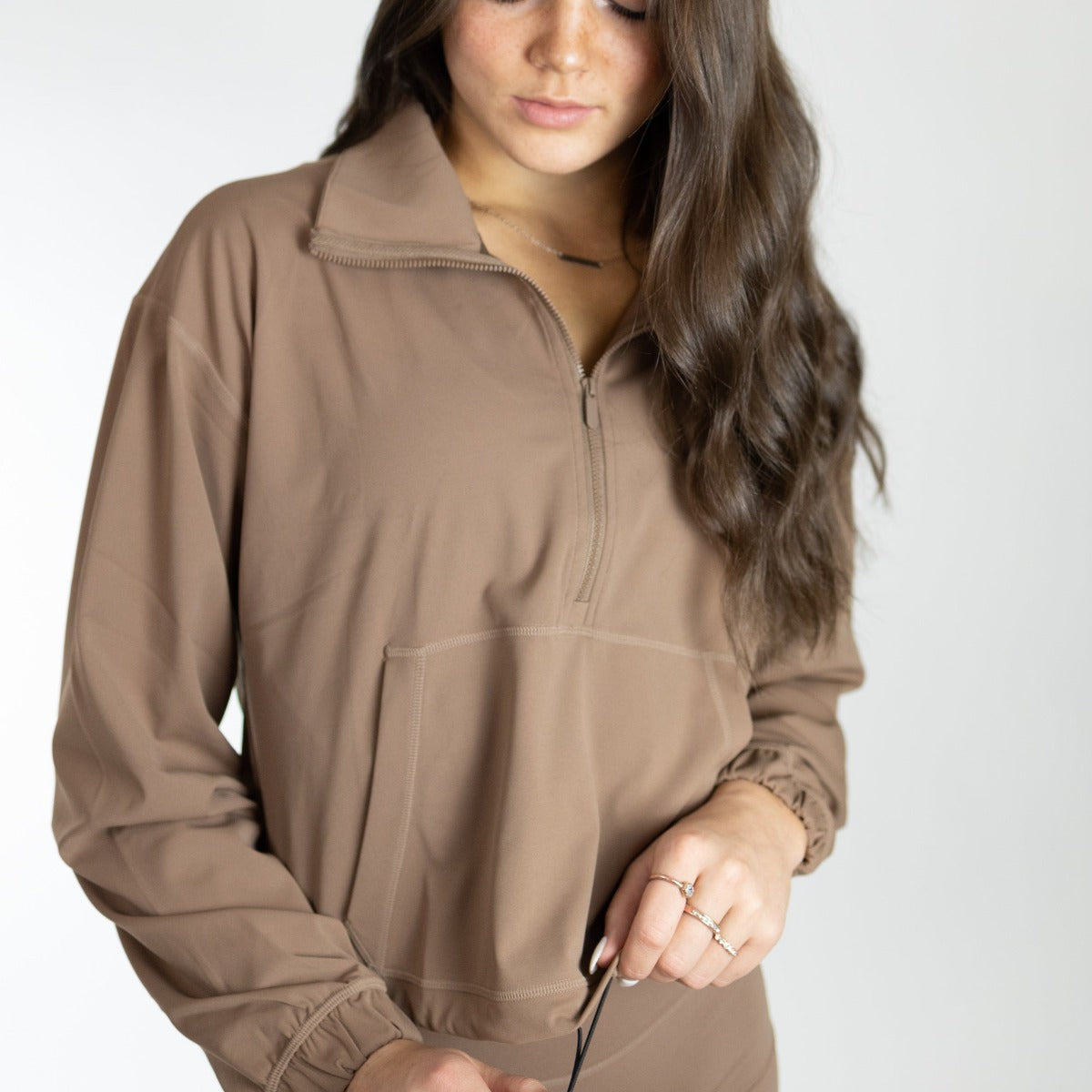 Model in a brown Ascend 1/4 Zip Jacket by DYM Athletics, demonstrating its comfortable fit and practical design with a half-zip feature.
