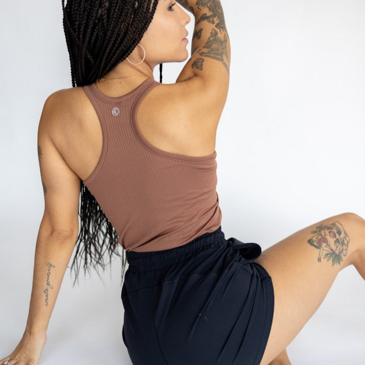 Back view of a model in the warm brown Restore Ribbed Comfort Tank with Built-in Bra by DYM Athletics, emphasizing its racerback design and comfort.