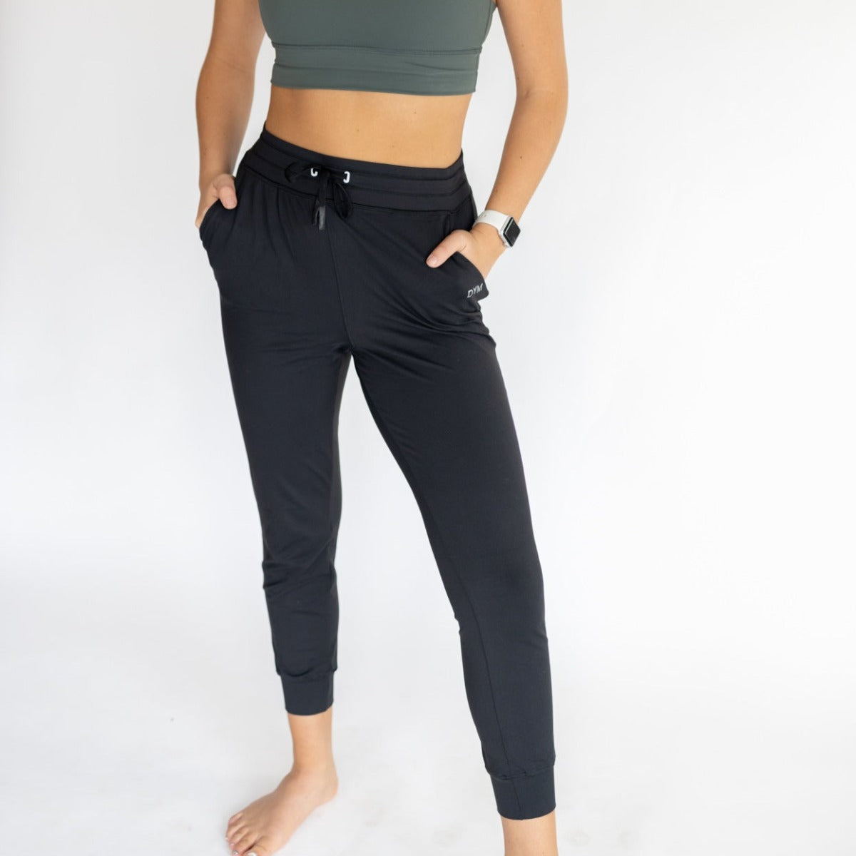 Close-up of a woman modeling Performance Pro Lightweight Active Jogger by DYM Athletics, demonstrating the sleek black joggers with hands in pockets.