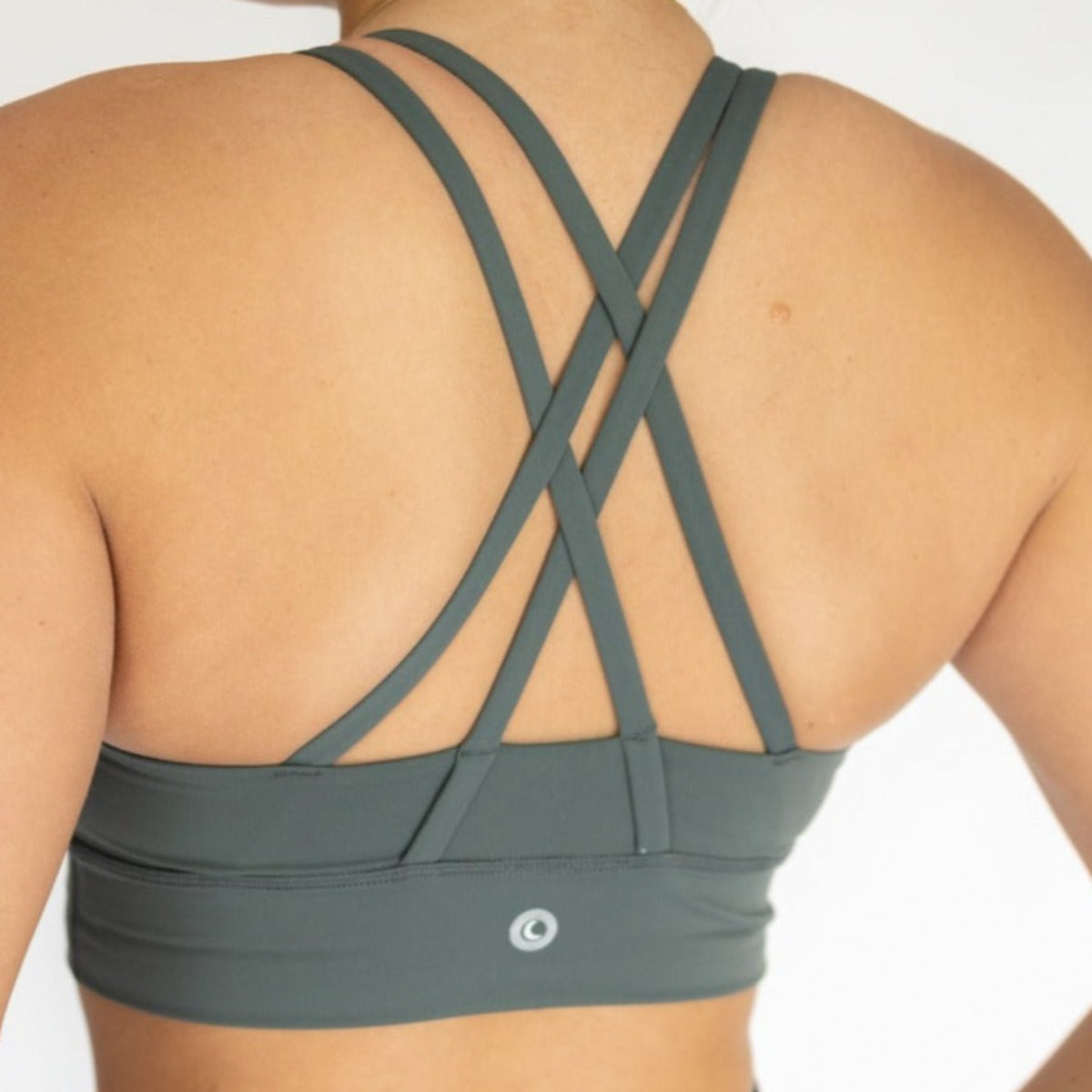Back view of a woman in the green Zone Bra by DYM Athletics, showcasing the supportive cross-back design for athletic performance.
