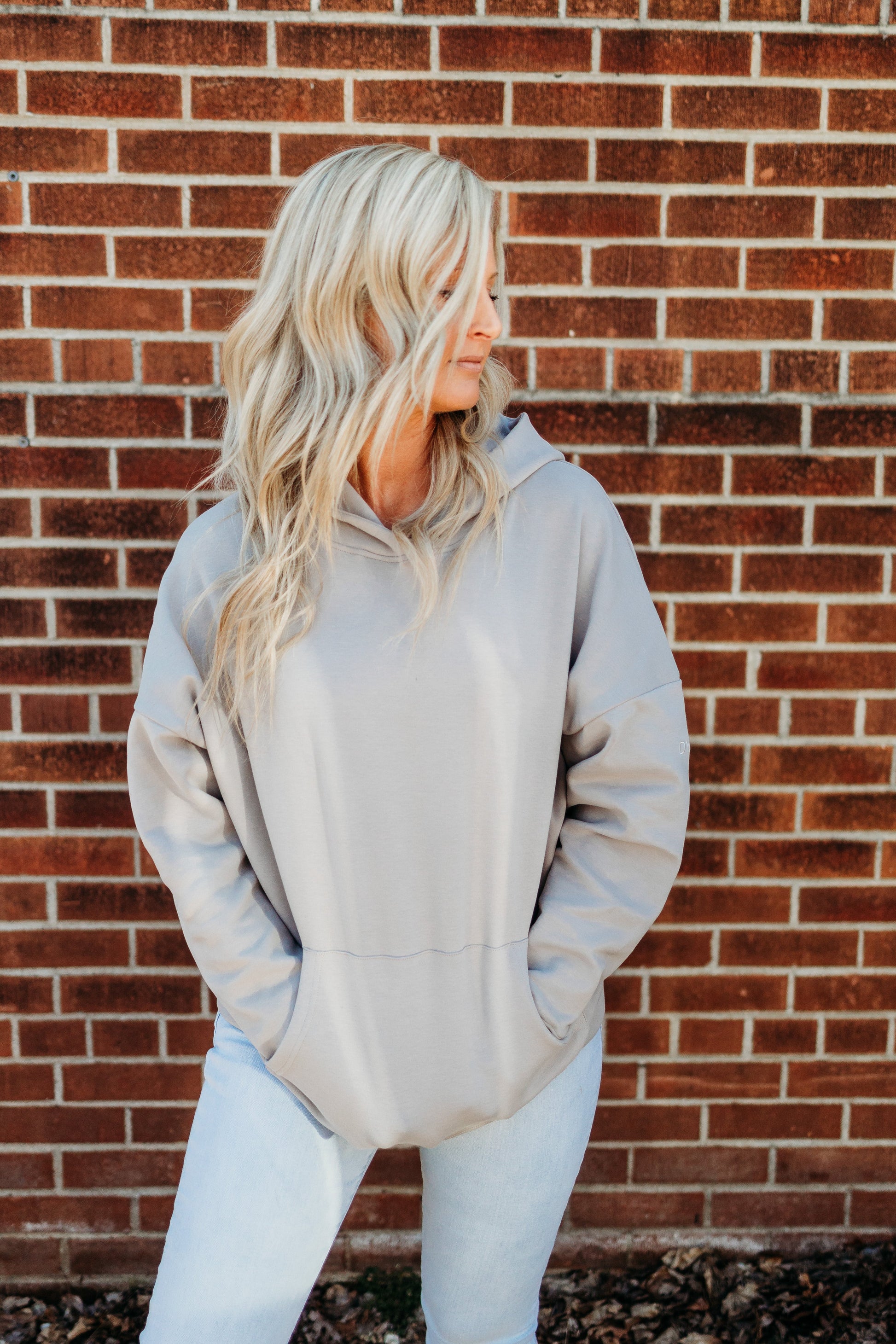 Model wearing the Cozy Up Boyfriend Hoodie in a casual pose against a brick wall, displaying the stylish design and relaxed fit by DYM Athletics.