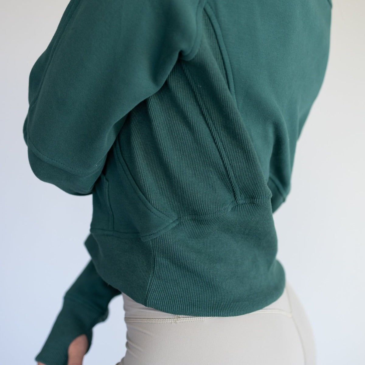Side view of a woman in a dark green Cozy Up Full Length 1/2 Zip Sweatshirt by DYM Athletics, highlighting the stylish fit and ribbed detailing.
