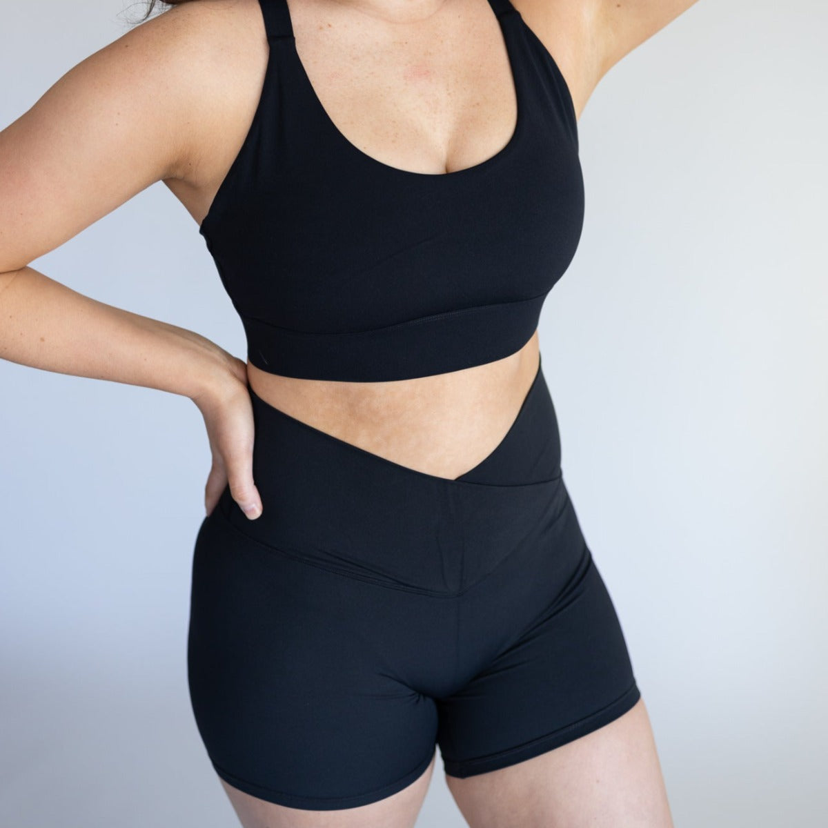 Model confidently wearing DYM Athletics Flex & Flow 4" V-Waist Shorts in black, paired with a matching sports bra, highlighting the flattering waist design.