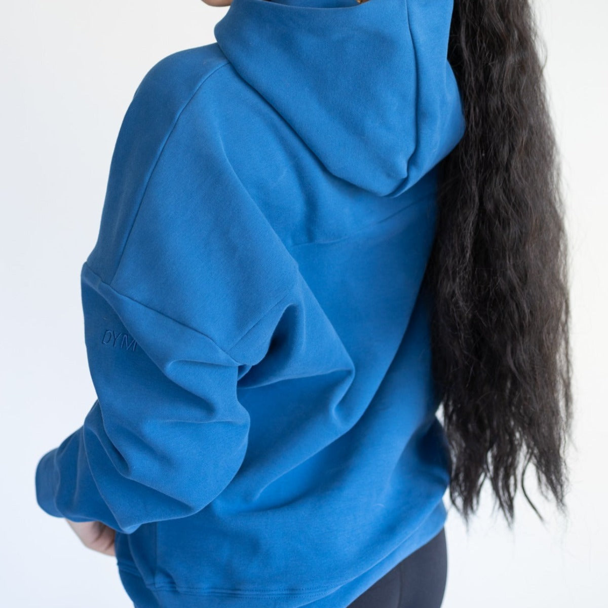 Back view of a model wearing the Cozy Up Boyfriend Hoodie in blue from DYM Athletics, showcasing its oversized fit and spacious hood.