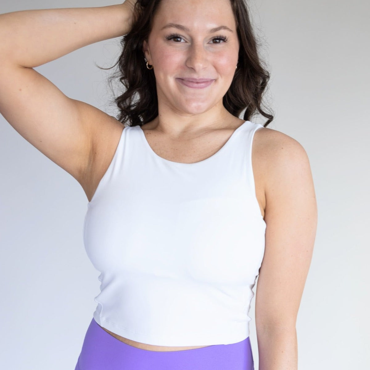 Smiling woman in a white DYM Athletics Bliss High Neck Bra with Scoop Back, showcasing its medium support and chic design, perfect for active wear.