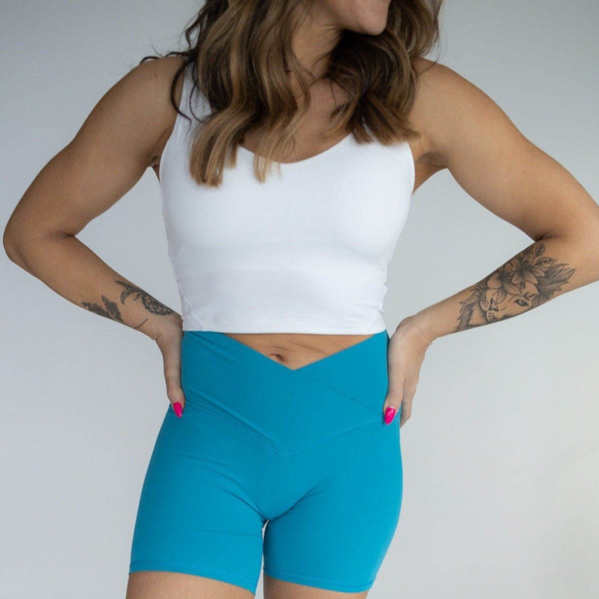 Model displaying DYM Athletics Flex & Flow 4" V-Waist Shorts in teal, highlighting the seamless design and trendy V-waist for a flattering look during workouts.