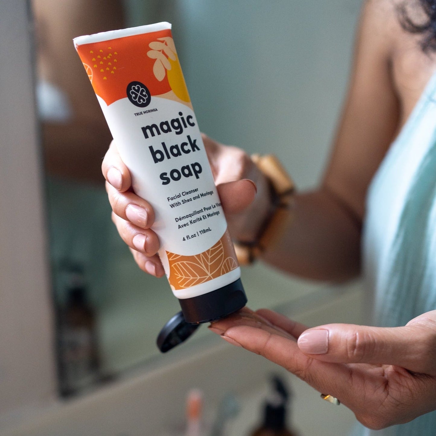 Person holding Magic Black Soap Facial Cleanser by True Moringa, showcasing its convenient tube packaging at a bathroom sink.