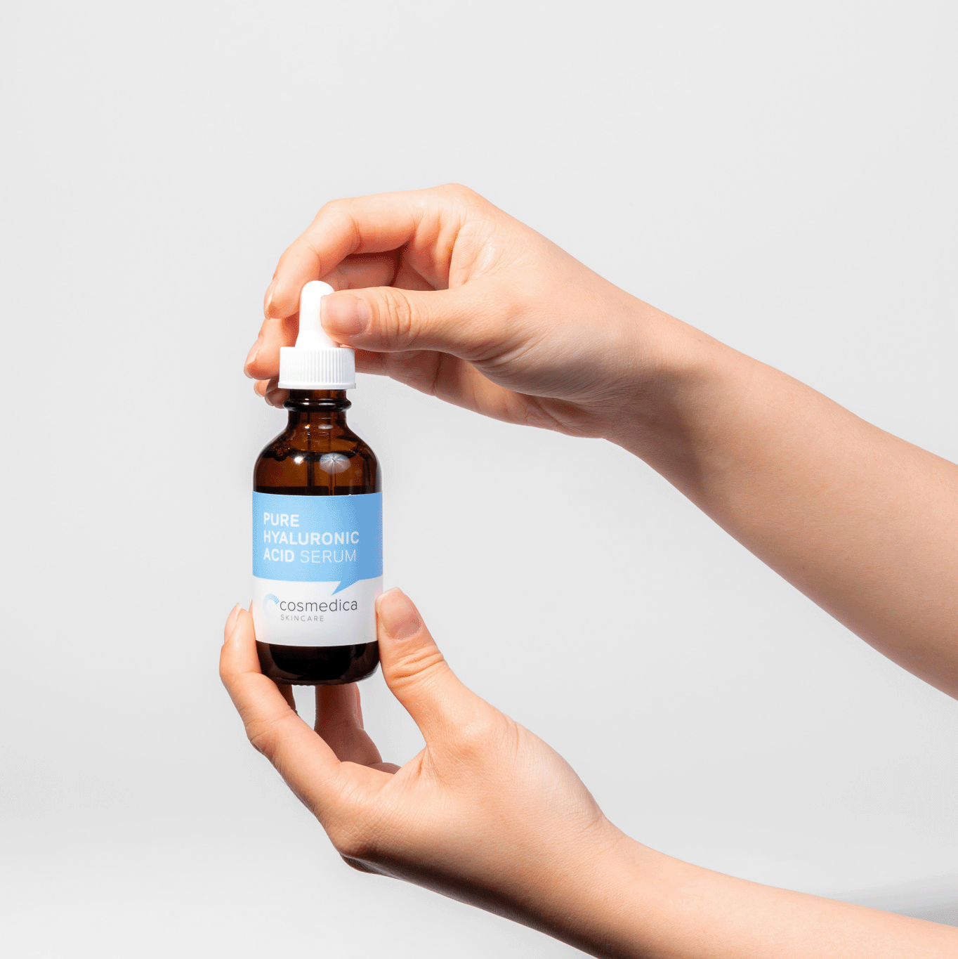 Hand holding the Pure Hyaluronic Acid Serum from the Hyaluronic + Vitamin C Serum Set by Cosmedica Skincare against a clean background.