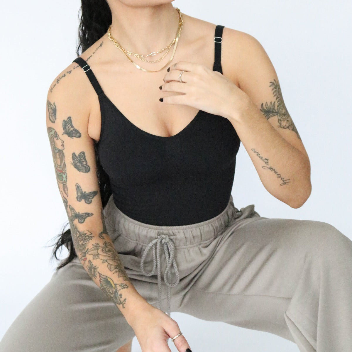 Model wearing the DYM Athletics Sculpting Comfort Bodysuit in black, seated in a stylish pose, demonstrating the bodysuit's versatility.