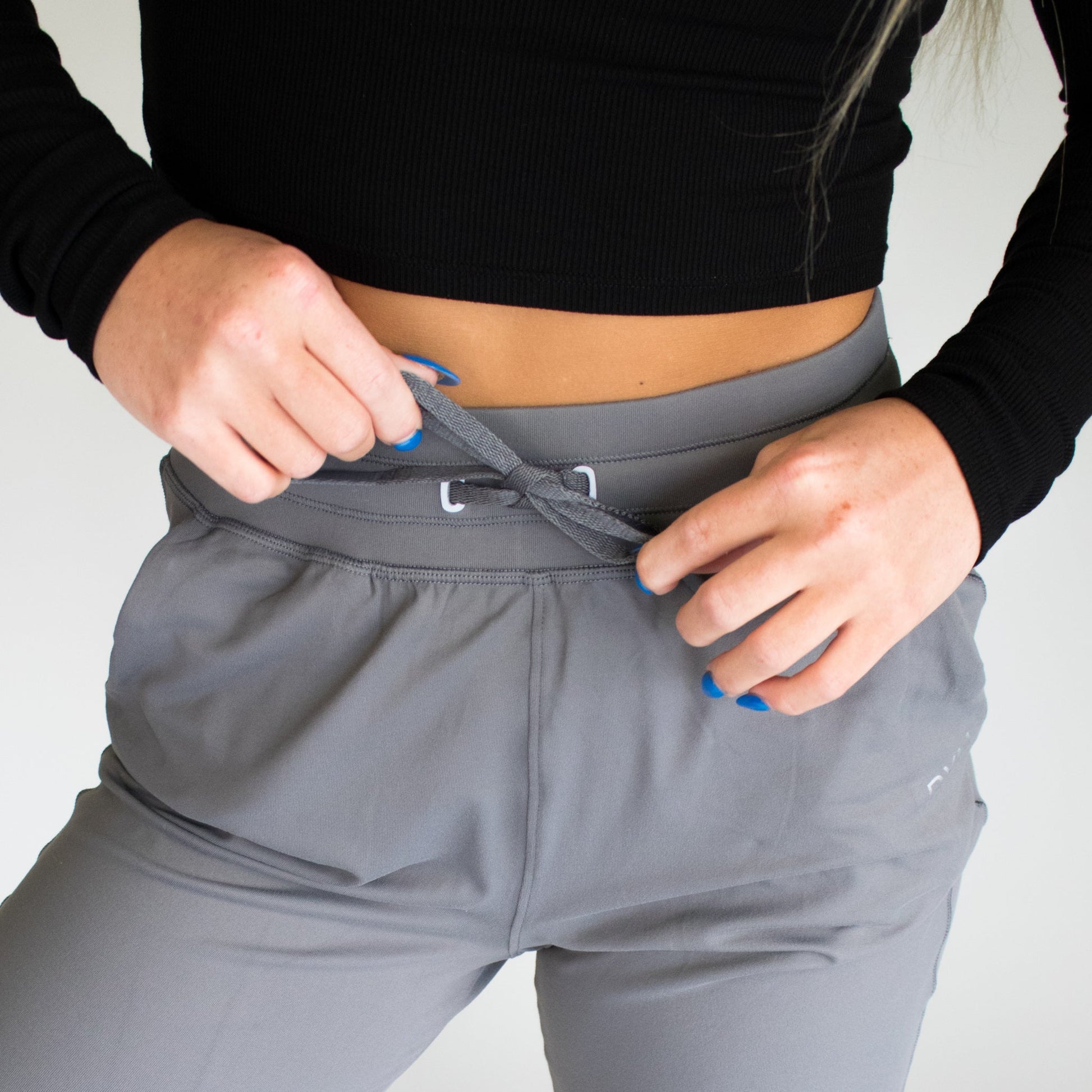 Detailed view of a woman tightening the drawstring on gray Performance Pro Lightweight Active Jogger by DYM Athletics, showcasing comfort and functionality.