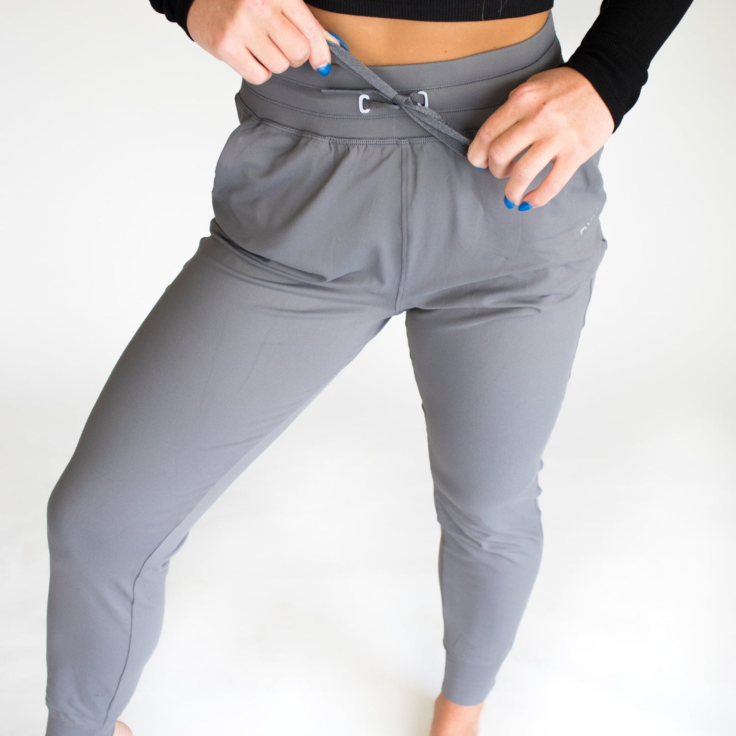 A woman adjusting the waistband of gray Performance Pro Lightweight Active Jogger by DYM Athletics, highlighting the customizable fit.