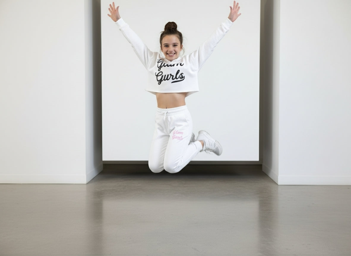 A young girl joyfully jumping in a Customized Glam Gurls Cropped Hoodie with Puff Print while wearing matching joggers, showcasing the soft and comfy style in white by Glam Gurls.