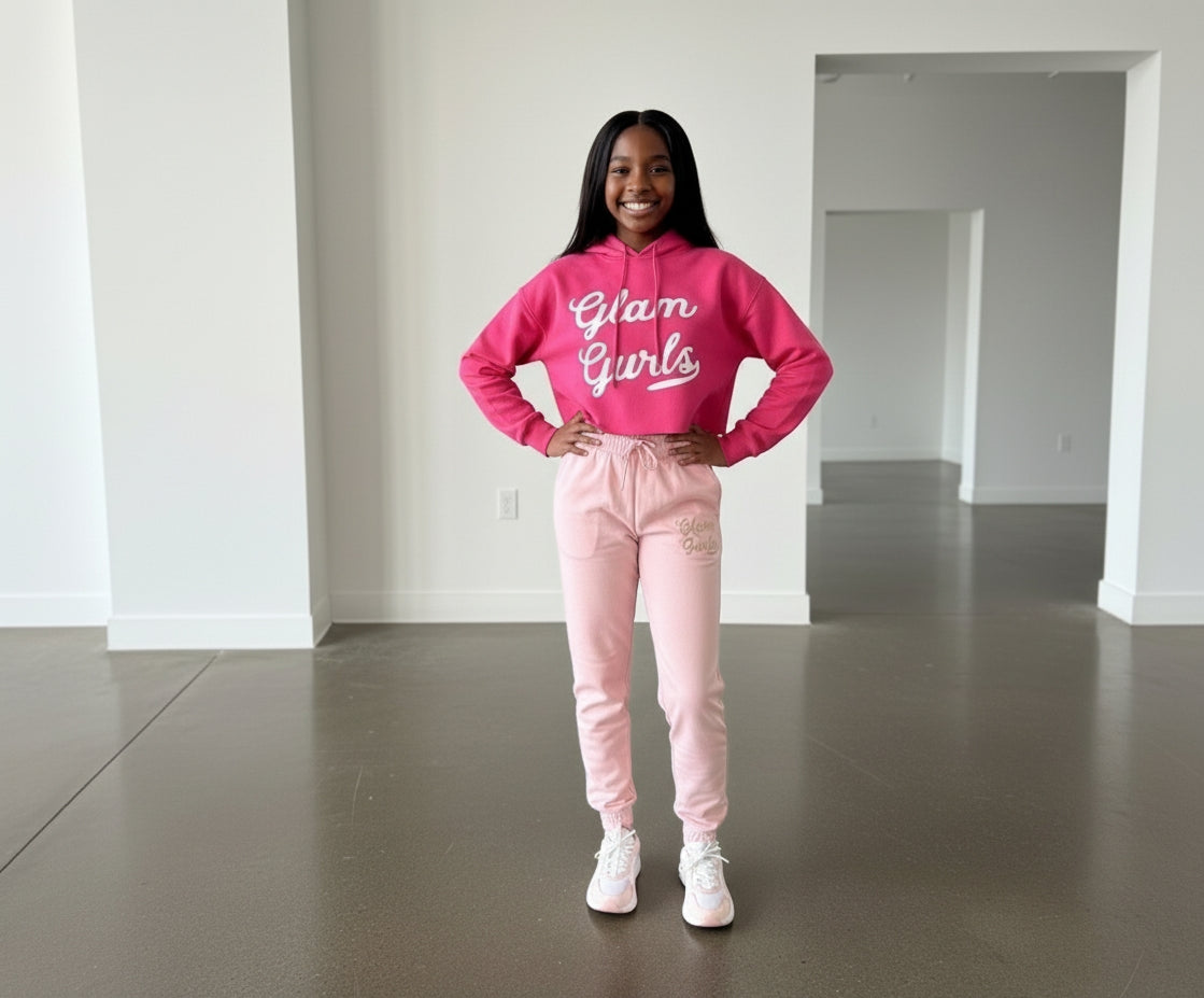 A young girl standing confidently in a pink Customized Glam Gurls Cropped Hoodie with Puff Print, paired with pink joggers, emphasizing comfort and style by Glam Gurls.
