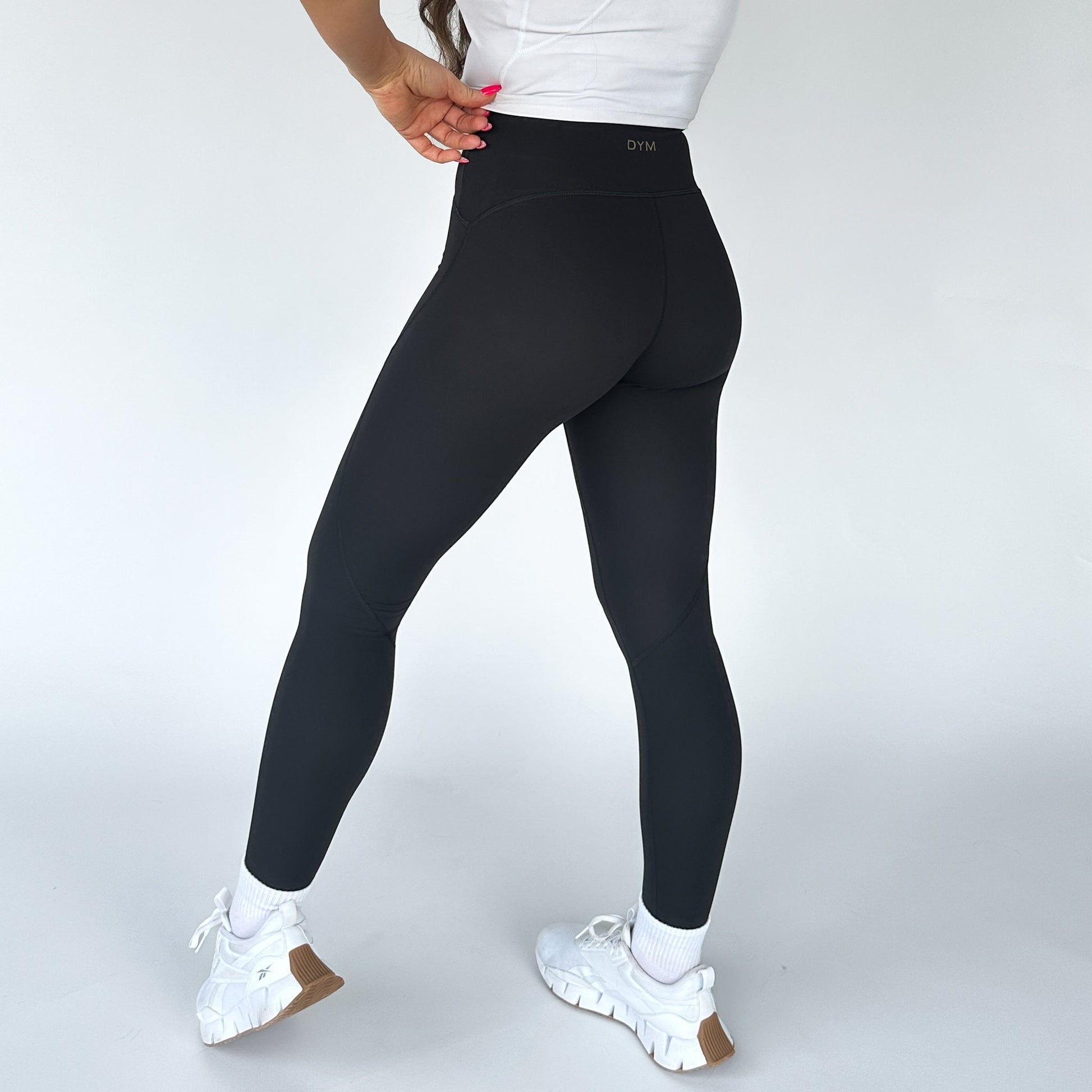 Back view of a model wearing DYM Athletics Trainer Muscle Tone Legging, showcasing the flattering fit and high-waist design, paired with stylish white sneakers.