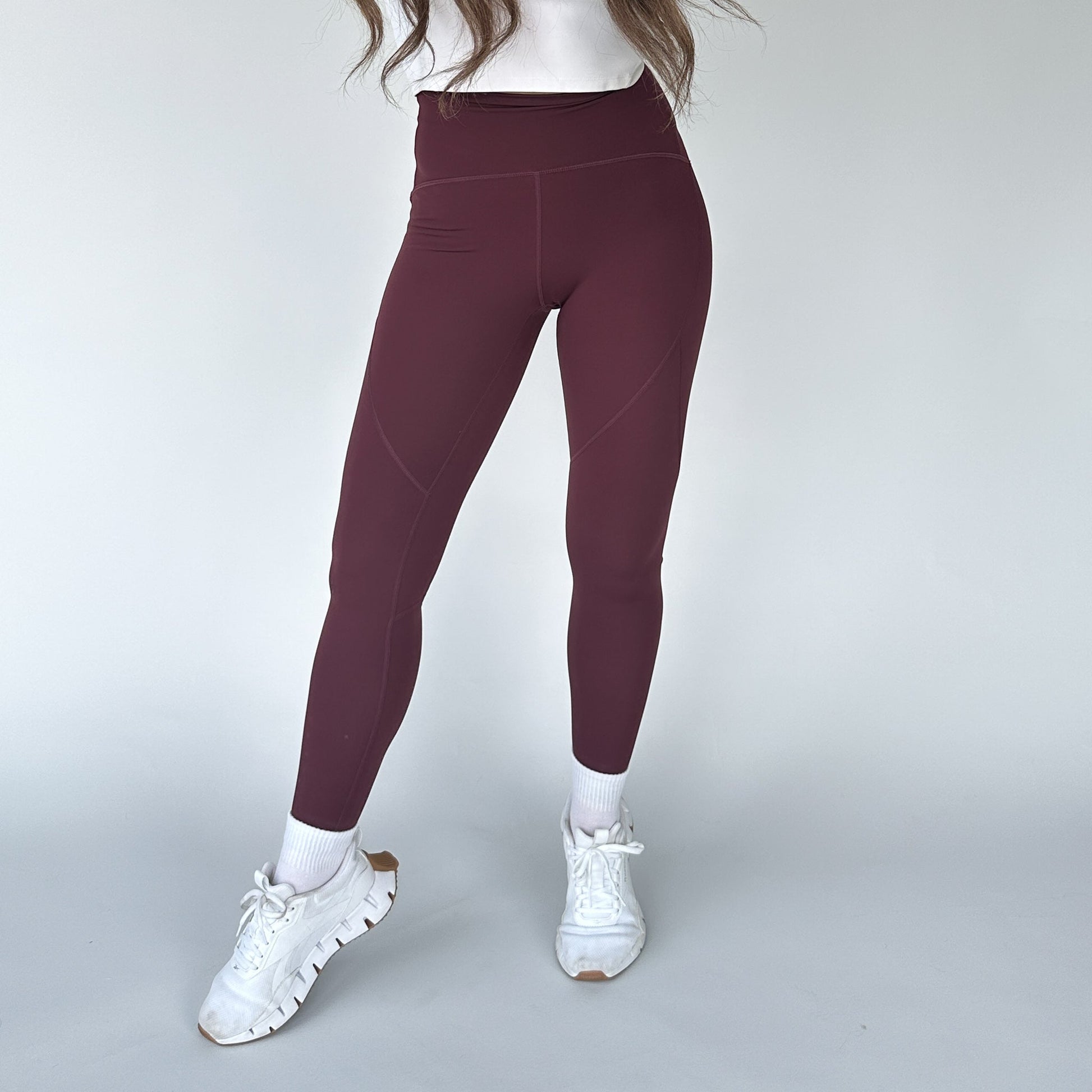 Woman demonstrating the front view of Trainer Muscle Tone Legging by DYM Athletics in maroon, designed for high-performance workouts.