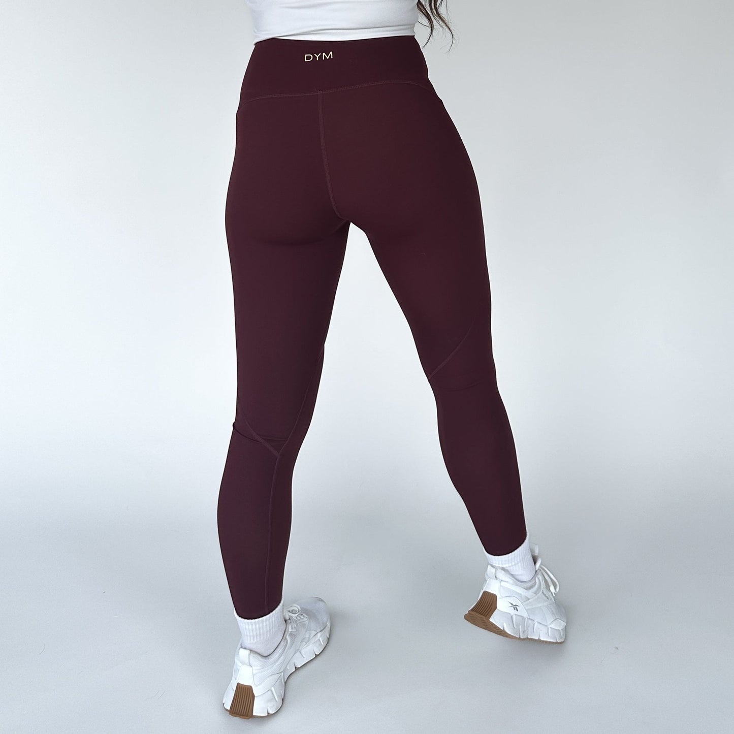 Back view of a woman in maroon Trainer Muscle Tone Legging by DYM Athletics, showing the high-waist fit and supportive design.