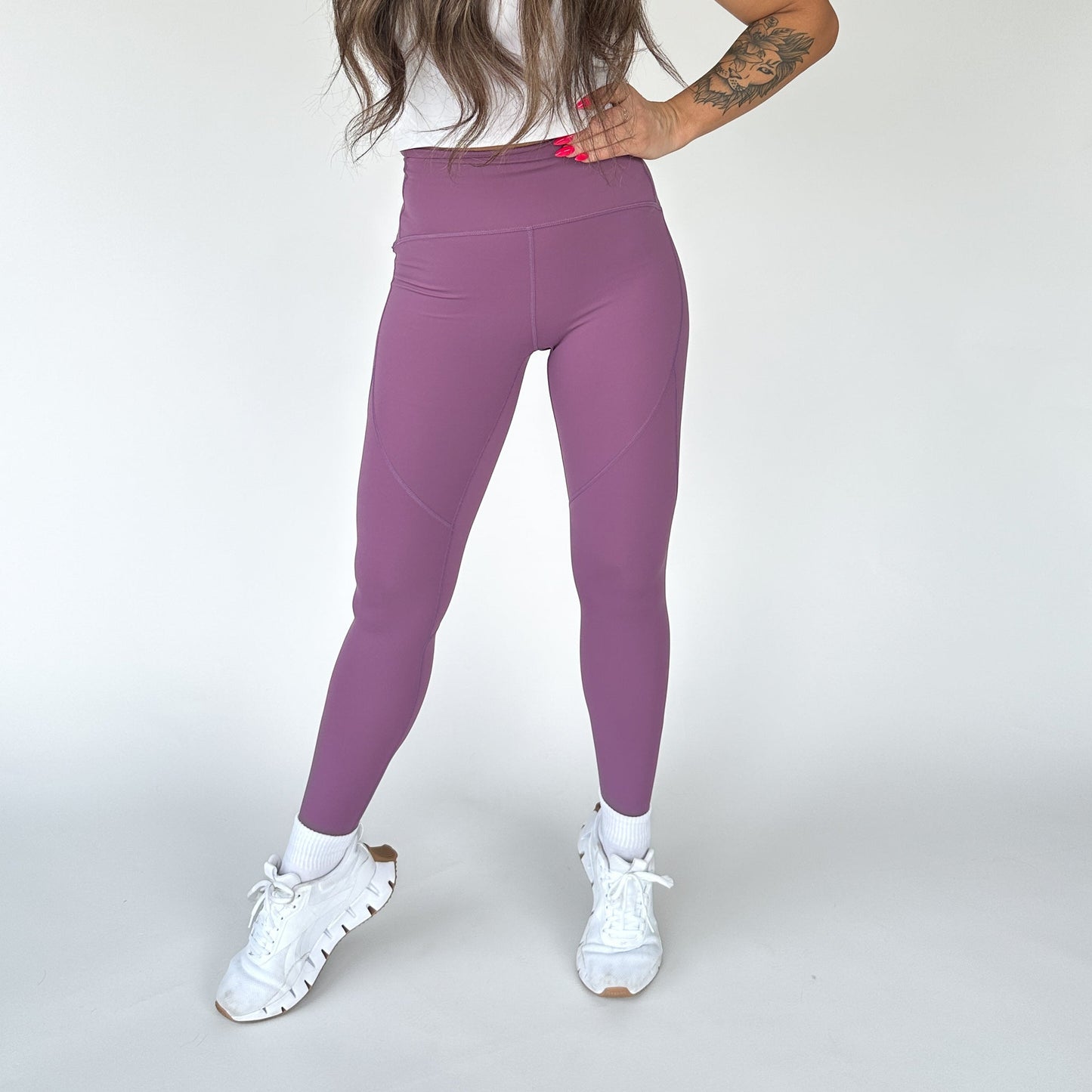 Woman standing confidently in the front view of Trainer Muscle Tone Legging by DYM Athletics, showcasing its stylish purple color and high-waist design.