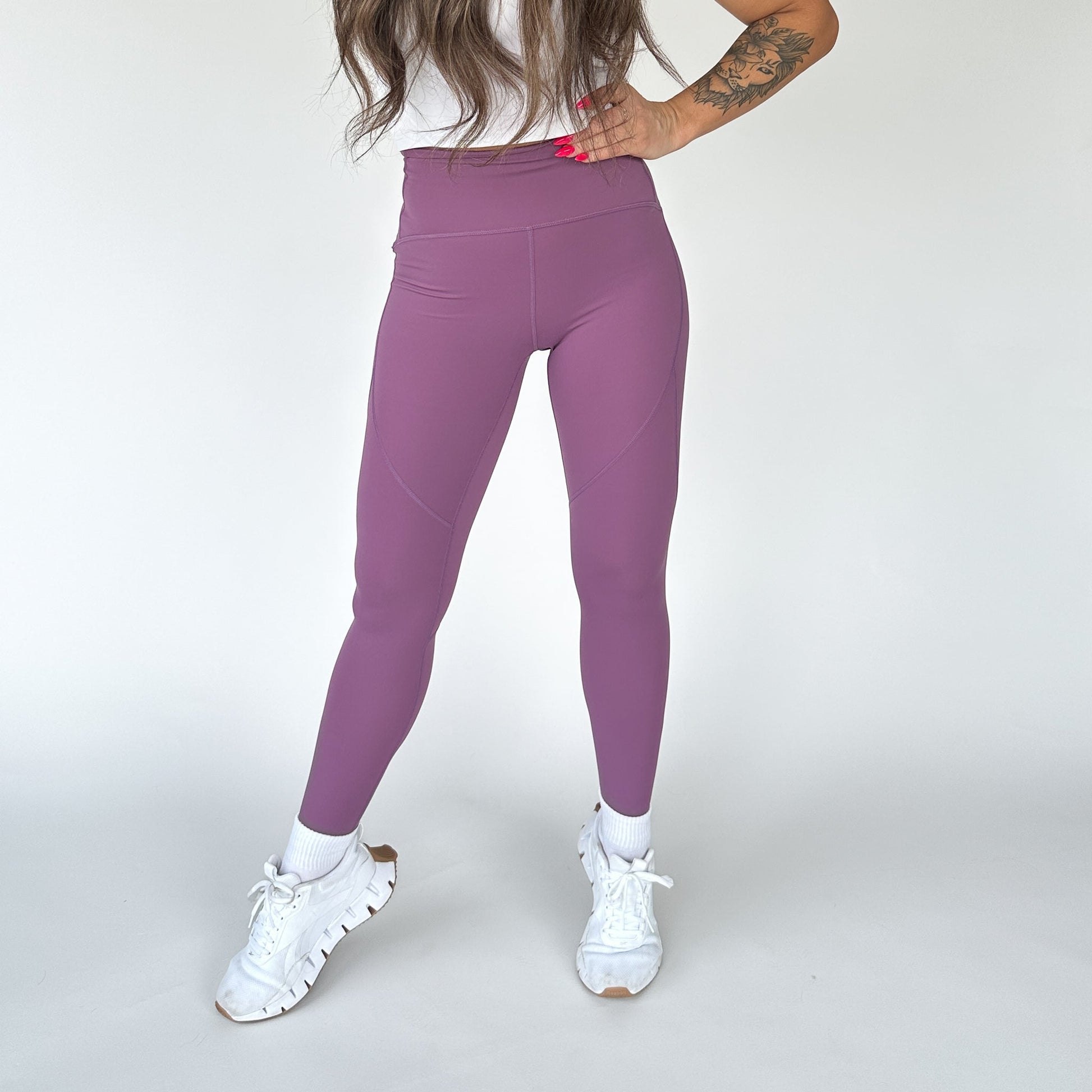 Woman standing confidently in the front view of Trainer Muscle Tone Legging by DYM Athletics, showcasing its stylish purple color and high-waist design.