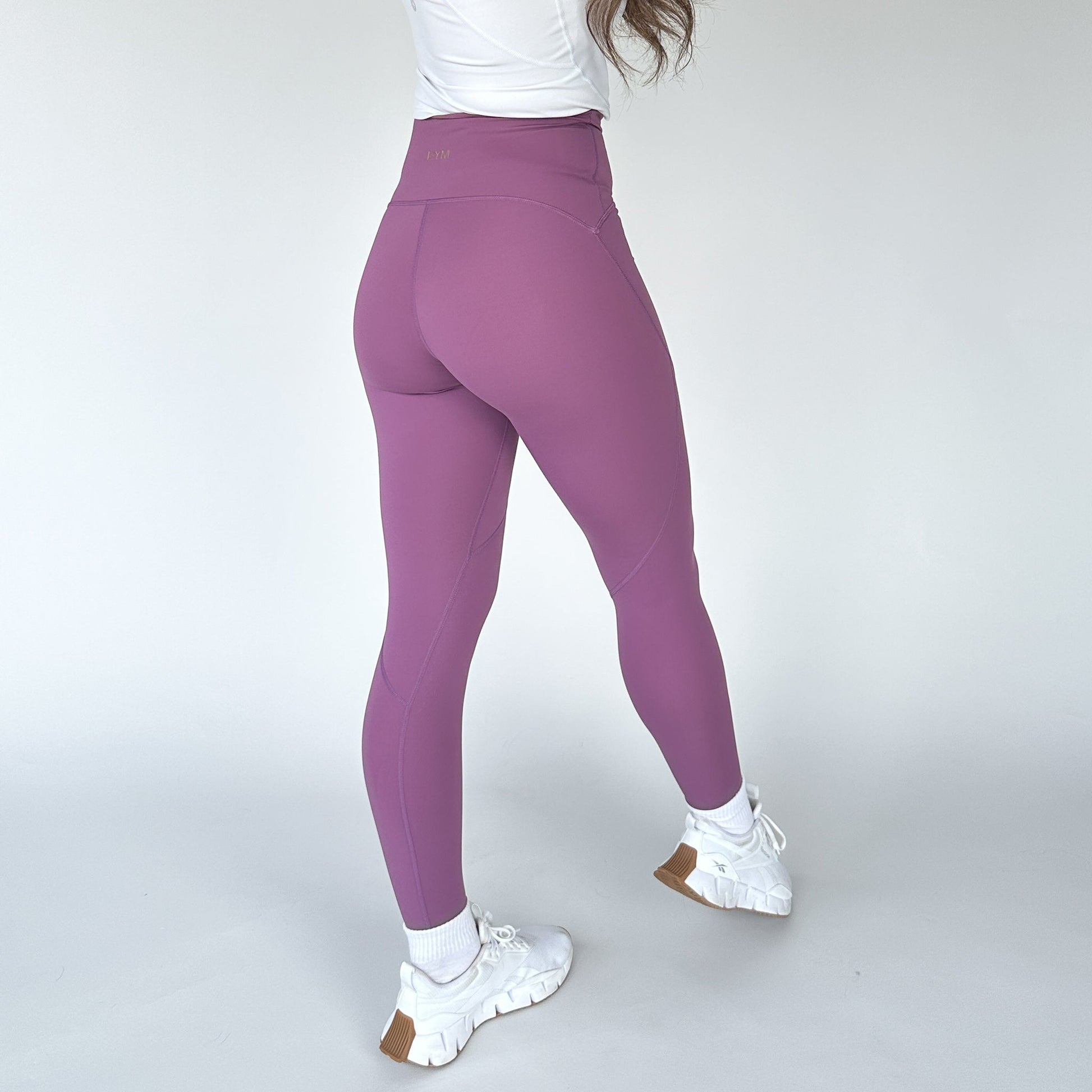 Close-up of a woman wearing the back view of Trainer Muscle Tone Legging by DYM Athletics in purple, highlighting the sculpting seams.
