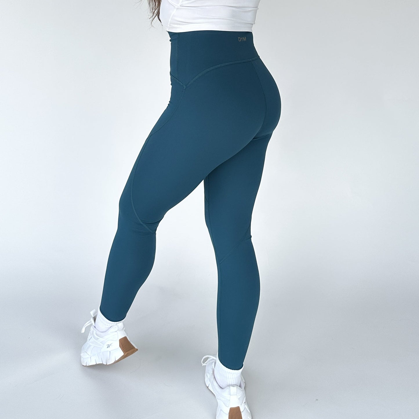 Woman showing the back view of Trainer Muscle Tone Legging by DYM Athletics, featuring a high-waist design and a sleek fit.