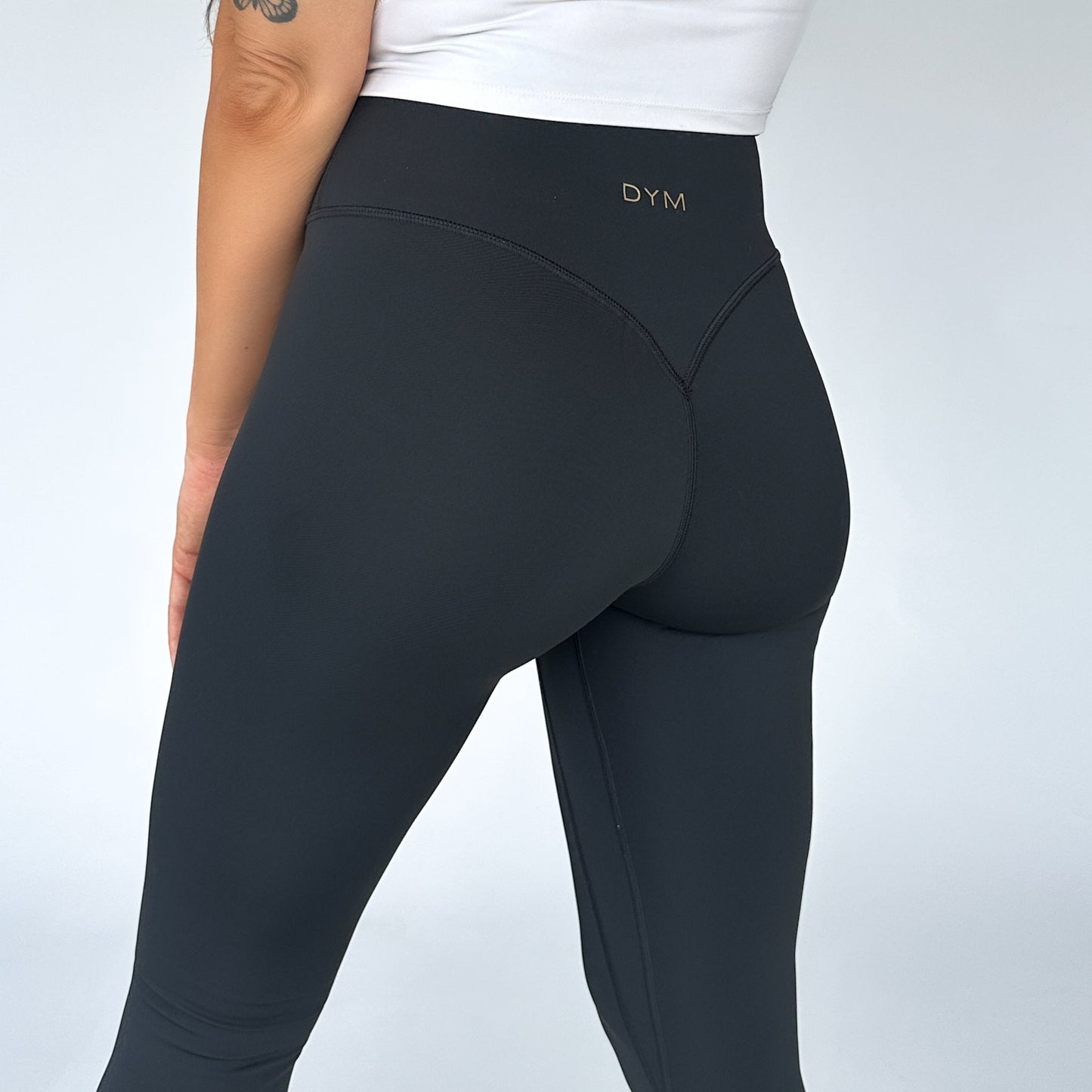 Close-up view of a model wearing High Society Sculpting Legging from DYM Athletics, highlighting the deep V booty seam and chic gold logo.