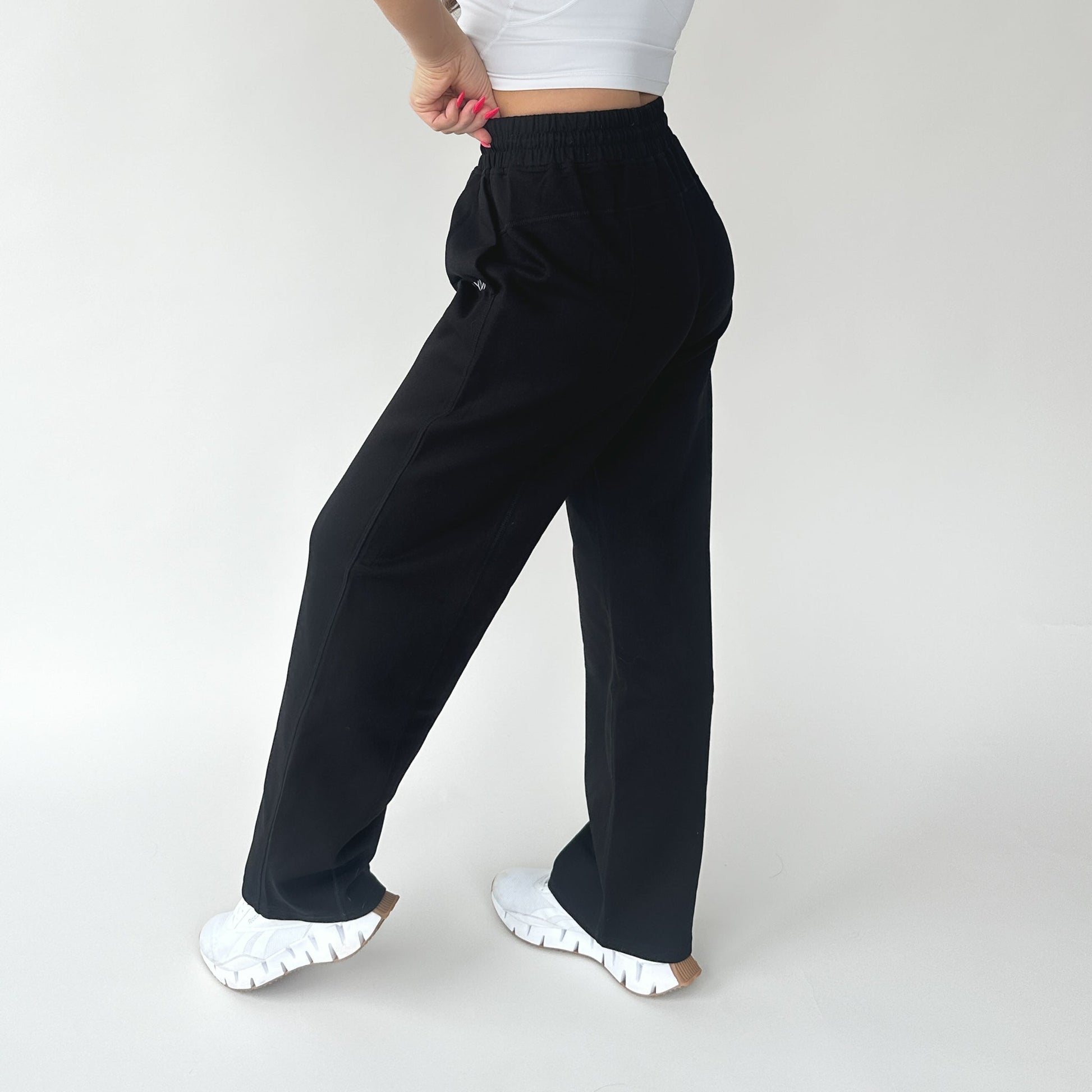 Back view of a woman in Relax Wide Leg Sweatpant with Cinch Drawstring by DYM Athletics in black, highlighting the cinch drawstring and comfy design.