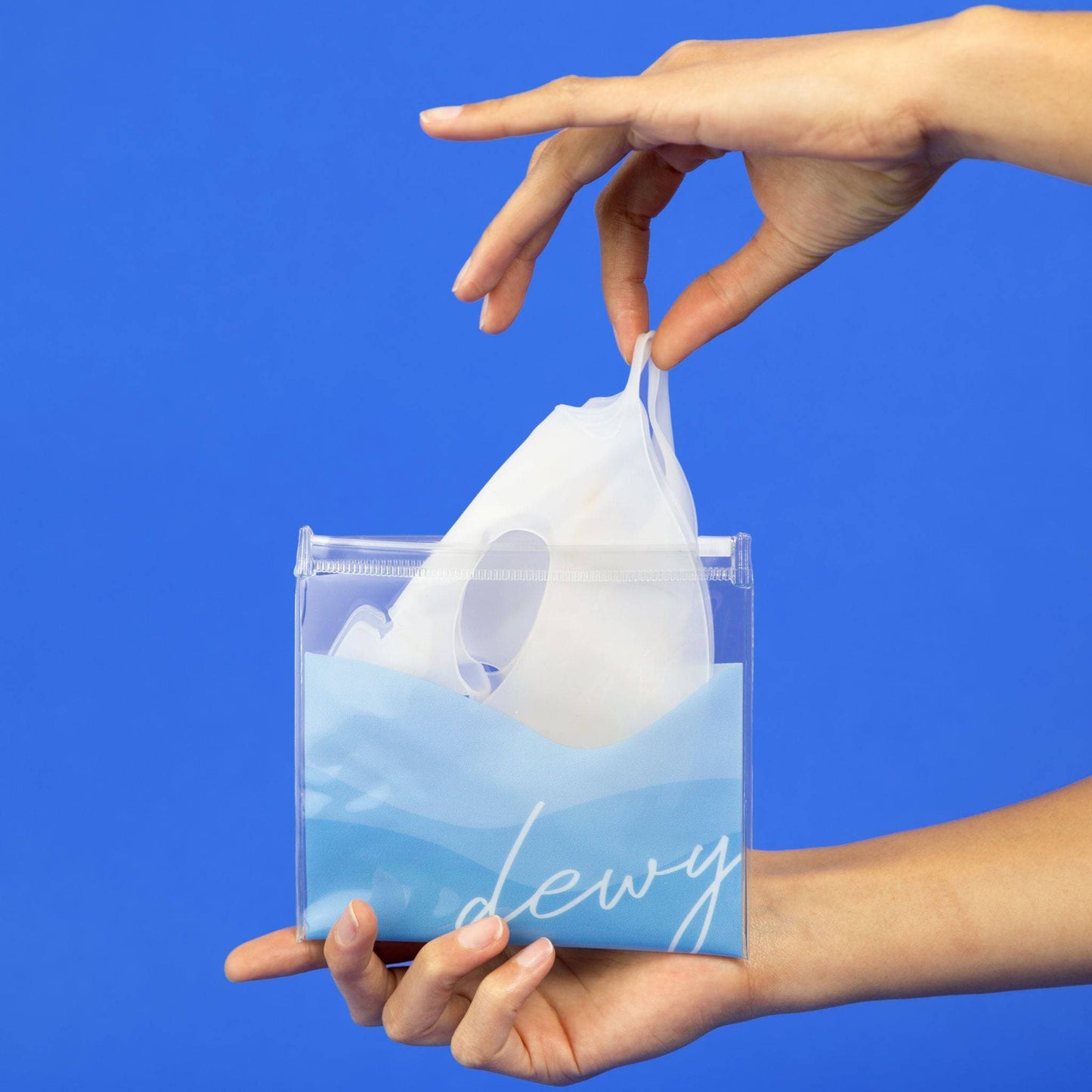 Close-up of hands retrieving the Reusable Silicone Hydro Mask by Cosmedica Skincare from a stylish blue pouch, emphasizing its convenience and eco-friendliness.