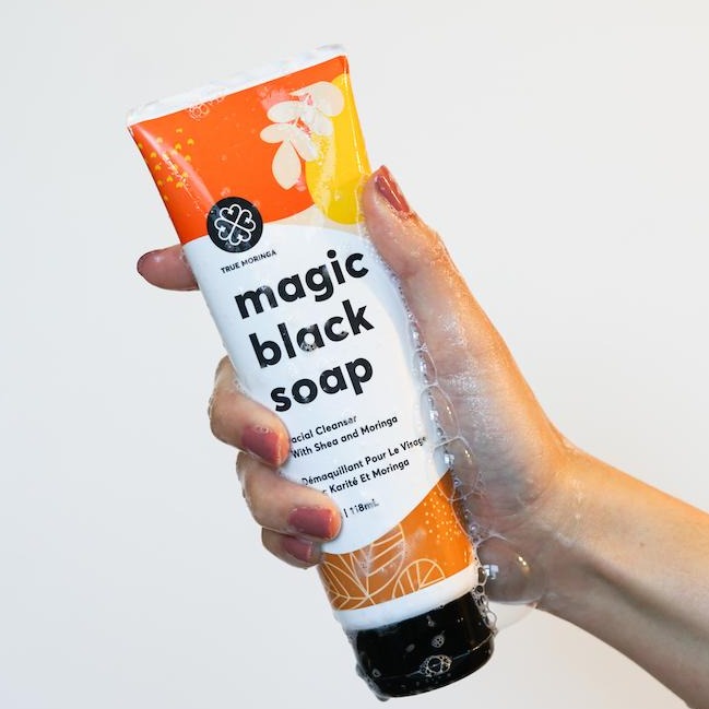 Person holding the Magic Black Soap Facial Cleanser by True Moringa with a bubbly texture, showcasing its creamy and hydrating formula for healthy skin.