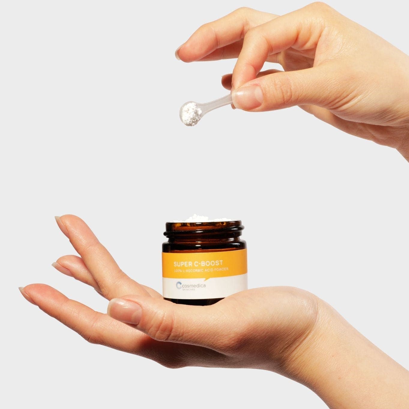 A hand holding a spoonful of Cosmedica Skincare Super C-Boost, highlighting its versatility as a topical Vitamin C powder.